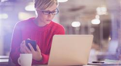 An email marketer looking intently between her cellphone and her laptop