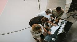 birds-eye view of four professionals standing over a laptop computer 