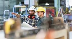 two men wearing hard hats discussing the blue print plans they're holding