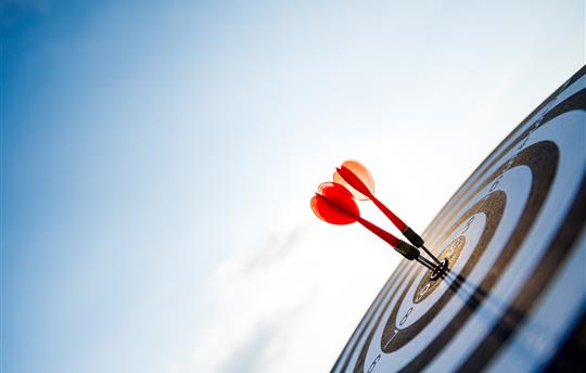 red dart hitting dart board with blue sky