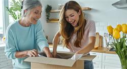 Happy senior woman and her adult daughter unpacking box while standing at the domestic kitchen