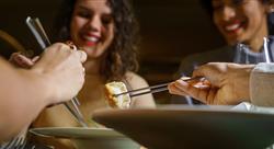 group of smiling young friends eating dim sum dumplings at a restaurant