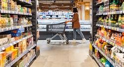 a woman with a cart walks between rows of shelves in a grocery store