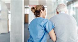 healthcare worker escorting elderly man down hospital hallway