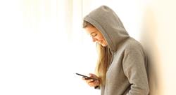 Side view portrait of a smiling young woman leaning on a white wall using a smartphone