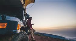 man leaning against his SUV and looking at phone as the sunsets near the ocean's edge