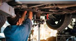 Mechanic repairing a car, mechanic inspects car suspension system and chassis with a torch-lite under the car.