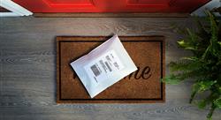 White padded envelope on a welcome mat on the porch of a house with a red door