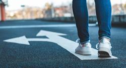 person in white tennis shoes standing on a white arrow painted on the ground in a parking garage